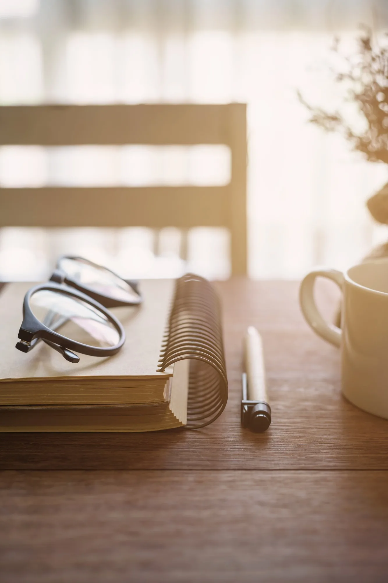Notebook and cup of coffee with sunlight on desk office